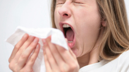 Woman sneezing and holding a white tissue