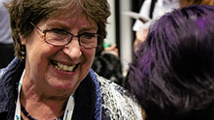 A person wearing glasses smiling and chatting.