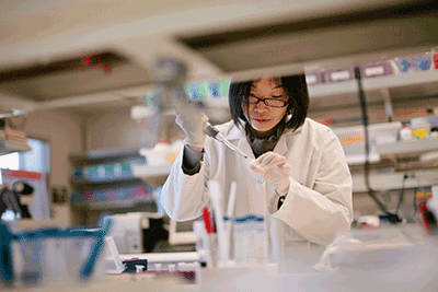 Scientist in a lab wearing PPE using a pipette.