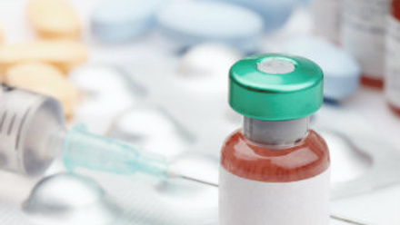 Medication bottle with syringe, bottles and pills in the background